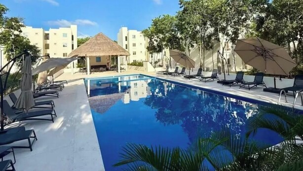 Una piscina con sillas de descanso y sombrillas, rodeada de edificios y árboles.
