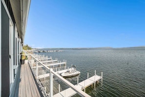 Una terraza con vista a un lago tranquilo, barcos amarrados y cielo despejado.