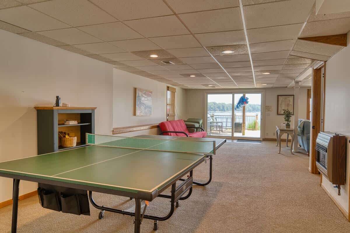 A room with a ping pong table, a fireplace, and a view of the outdoors.