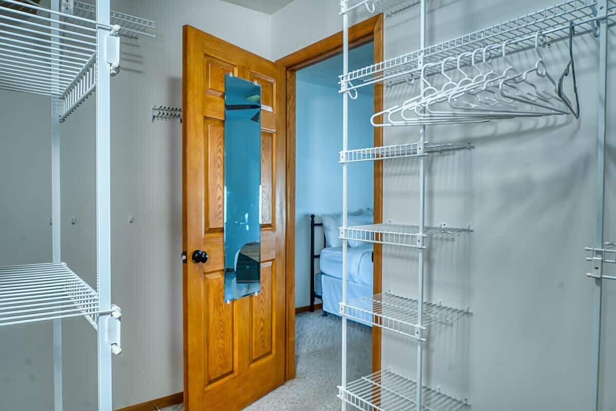 A room with a wooden door, white shelving units, and a bed with a blue cover.