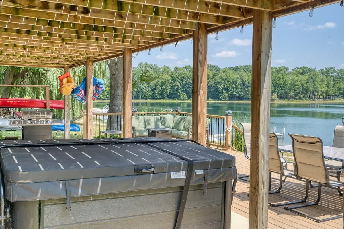 A covered outdoor deck with a hot tub, seating, and a view of a lake.