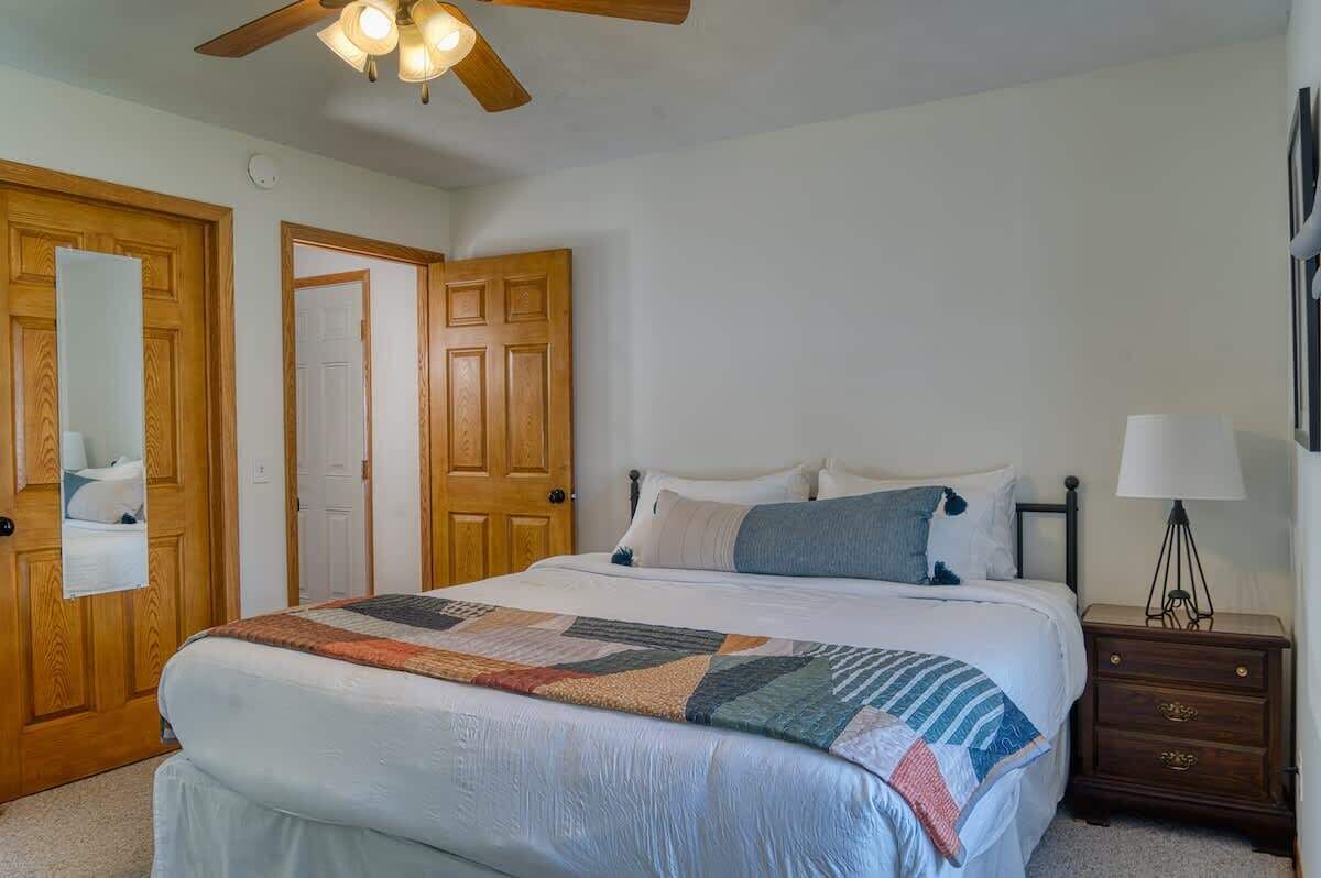 A bedroom with a bed, wooden doors, a ceiling fan, a nightstand, and a lamp.