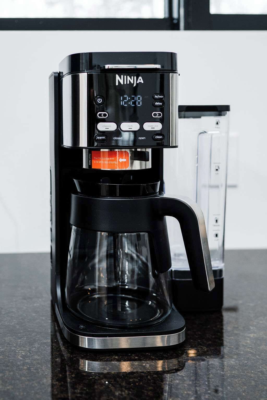 Una màquina de café Ninja negra amb pantalla digital, un recipient de vidre i un safata per al got sobre una superfície de cuina.