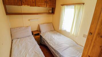 Un dormitorio de autocaravana compacto con dos camas, armarios de madera arriba, una ventana con cortinas y un enchufe.