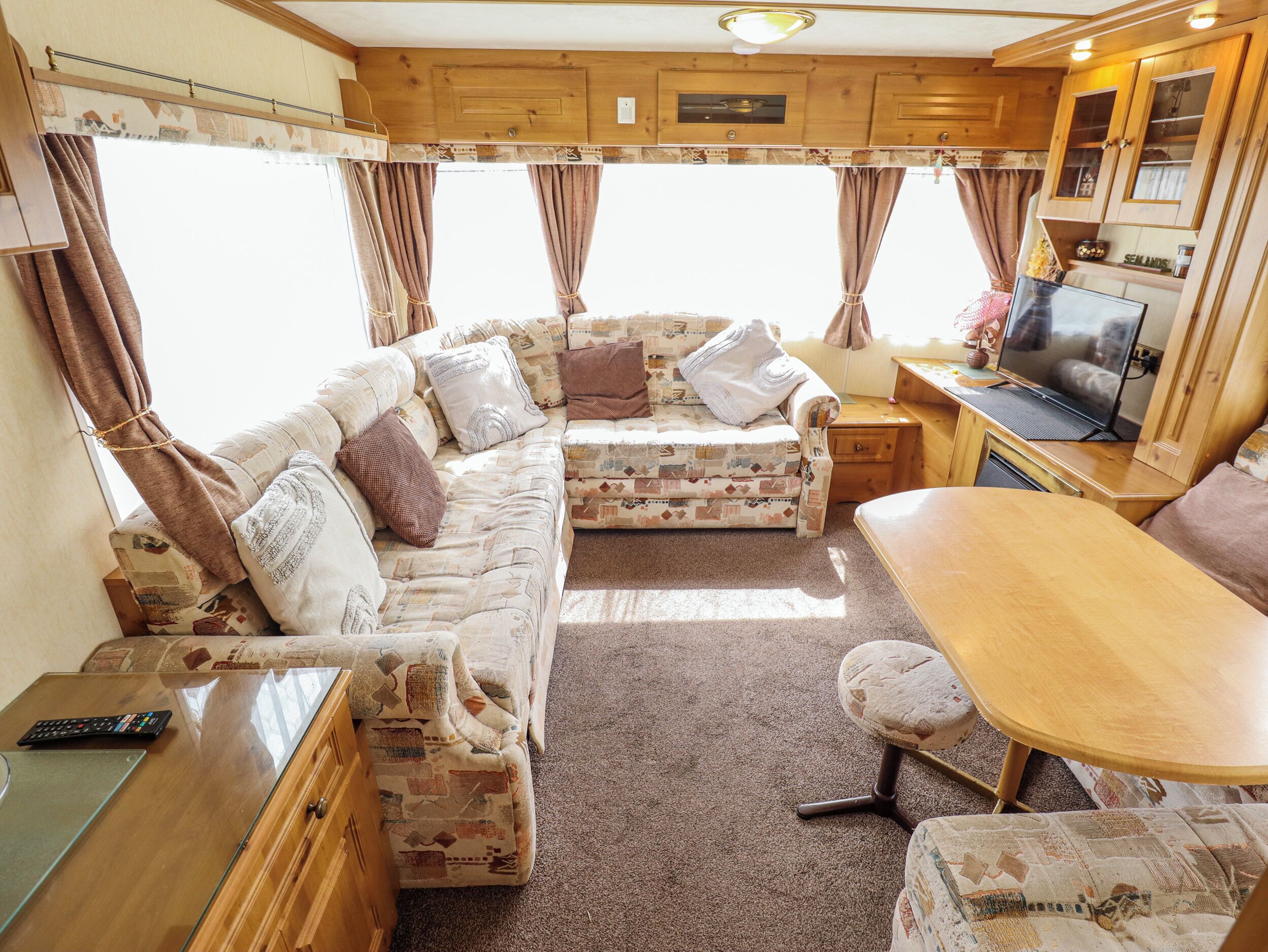 Interior acolhedor de uma motorhome, com sofá, mesa de jantar, televisão e armários de madeira.