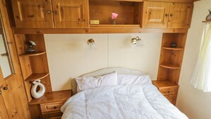 Un dormitorio con cabecera de madera, cama con ropa blanca, mesita de noche con un jarrón y estante con una flor.