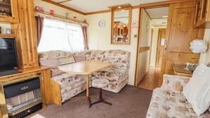 A cozy RV interior with a sofa, a small table, a TV, and a heater. - Caravan 25 (Skegness)