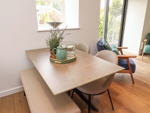 A dining area with a table, chairs, a bench, a potted plant, and a window with a view of greenery. - Snowdrop Cottage (Morpeth)