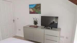 A bedroom with a bed, a TV on a cabinet, a painting on the wall, and a door. - Snowdrop Cottage (Morpeth)