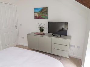 A bedroom with a bed, a TV on a cabinet, a painting on the wall, and a door. - Snowdrop Cottage (Morpeth)