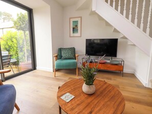 Ein modernes Wohnzimmer mit einem Holztisch, einem grünen Sessel, einem Fernseher und einer Treppe.