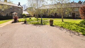 A stone building with a paved driveway, surrounded by well-maintained lawns and trees. - Snowdrop Cottage (Morpeth)