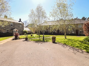A stone building with a paved driveway, surrounded by well-maintained lawns and trees. - Snowdrop Cottage (Morpeth)