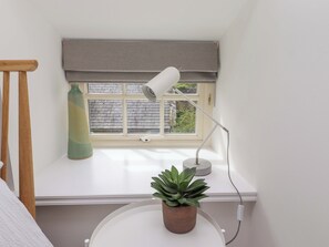 Ein Zimmer mit Fenster, Schreibtisch, Lampe, Pflanze und einem Holzsessel.