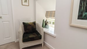 A corner room with a wicker chair, a radiator, a window with a view, and a framed picture on the wall. - Snowdrop Cottage (Morpeth)