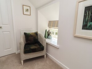 A corner room with a wicker chair, a radiator, a window with a view, and a framed picture on the wall. - Snowdrop Cottage (Morpeth)