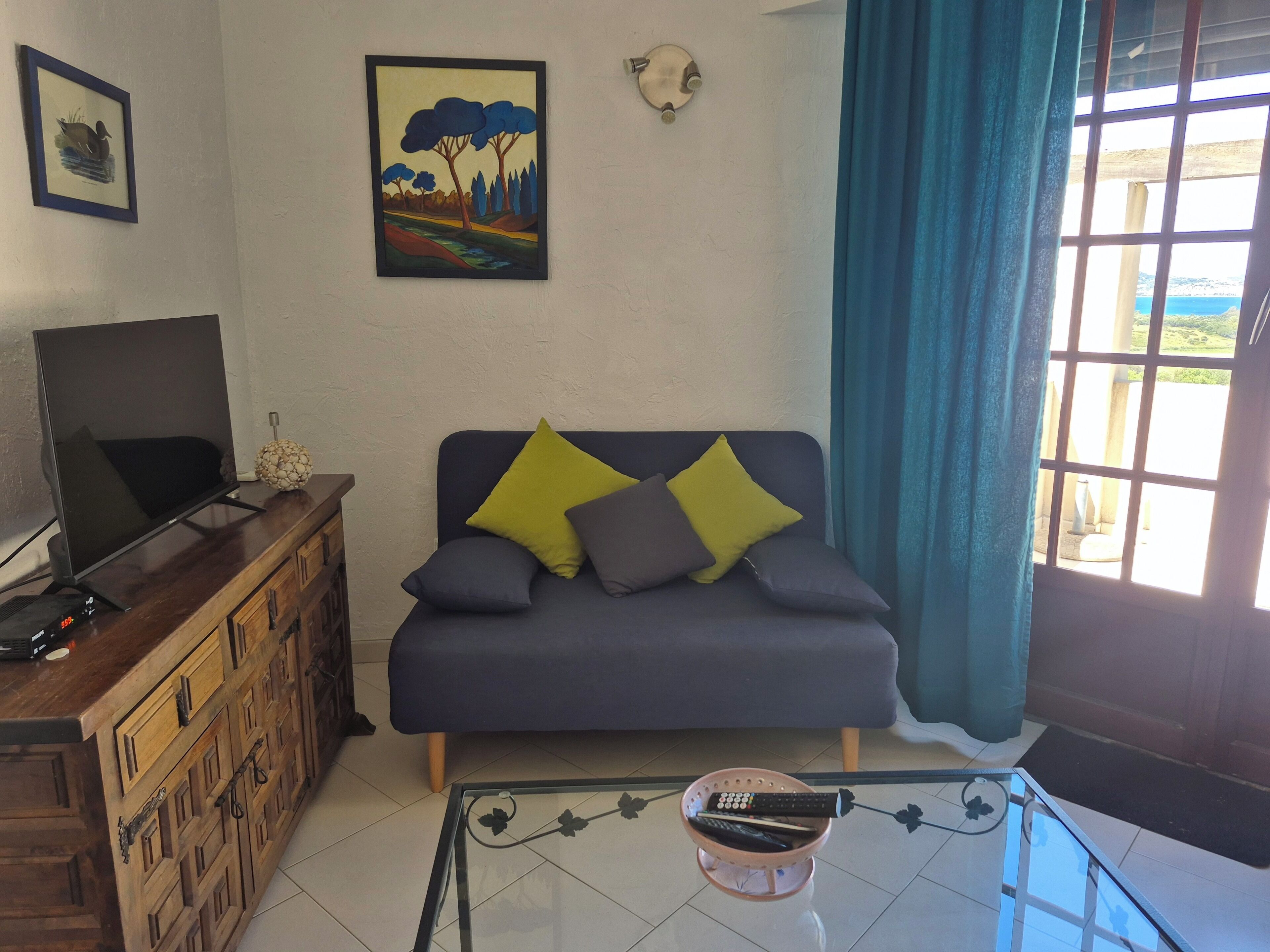 Uma sala de estar com sofá, televisão, mesa de centro e uma janela com cortinas.