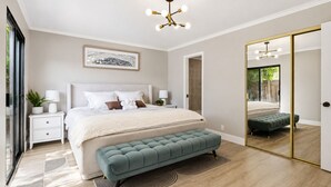 Quarto moderno com uma cama grande, mesas de cabeceira, um banco, um espelho e um lustre.