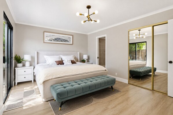 A modern bedroom with a large bed, bedside tables, a bench, a mirror, and a ceiling light fixture.