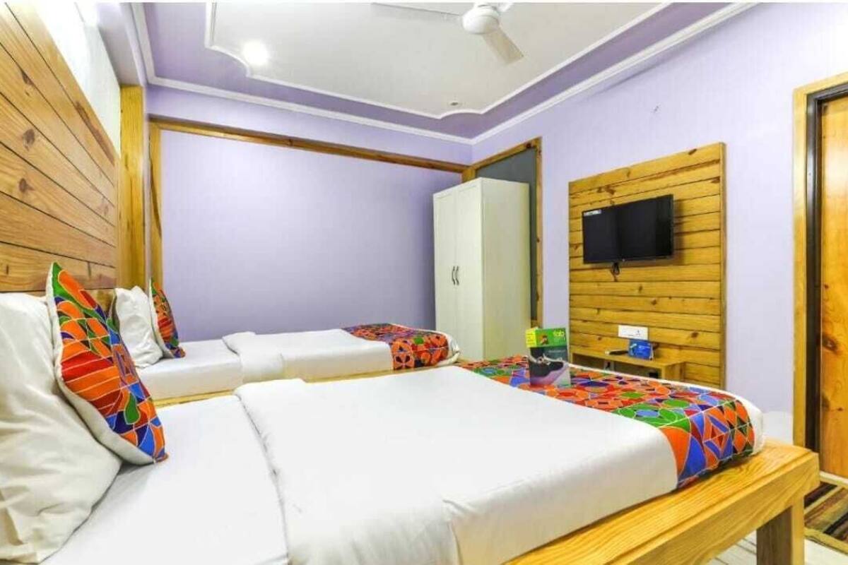 A room with two beds, a wardrobe, a television mounted on a wooden panel, and a ceiling fan.