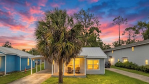 A row of single-story buildings with a central building featuring a porch with chairs, surrounded by well-maintained grass and a palm tree. - Beach House - St Joe Retreat (Port St. Joe)