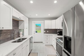 Una cocina moderna con armarios blancos, electrodomésticos de acero inoxidable y vistas a un paisaje verde a través de un ventanal.