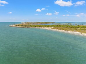 Un paisaje costero con una playa arenosa, aguas tranquilas y una barrera rocosa.