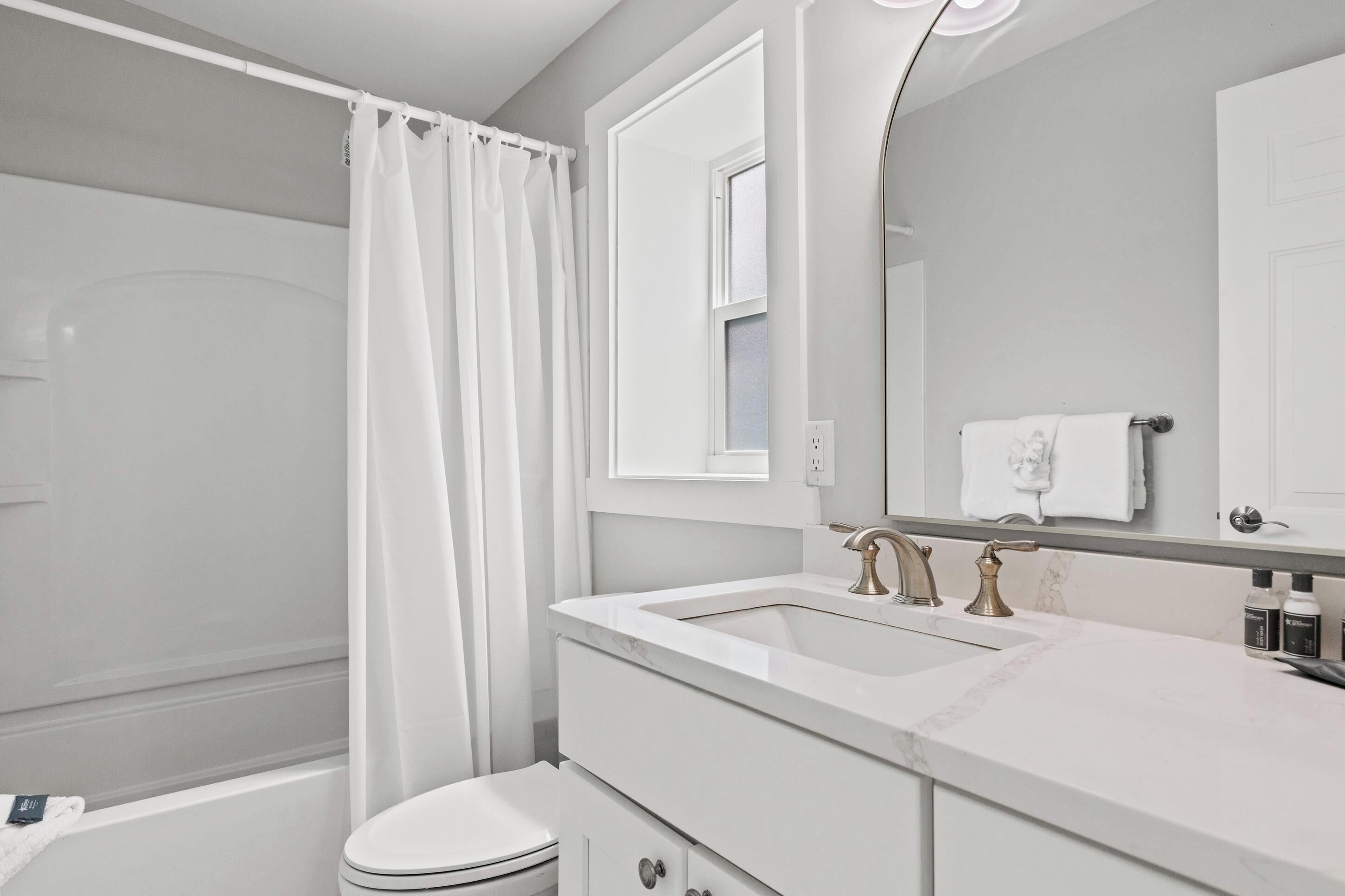 Baño con ducha, inodoro, lavabo de dos grifos y espejo.