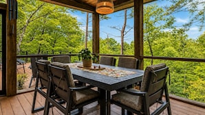 An outdoor wooden deck with a table and chairs, surrounded by trees.