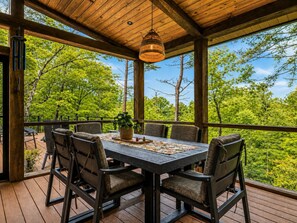 An outdoor wooden deck with a table and chairs, surrounded by trees.