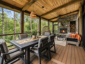 A covered outdoor seating area with a stone fireplace, wooden deck, and a view of the forest. - Luxury Treehouse Retreat | Bordering Gorges (Brevard)