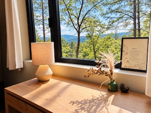 A window with a view of trees and mountains, a lamp, and a framed quote on a wooden table. - Luxury Treehouse Retreat | Bordering Gorges (Brevard)