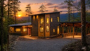 A modern two-story cabin with a stone facade, large windows, and a covered outdoor area.