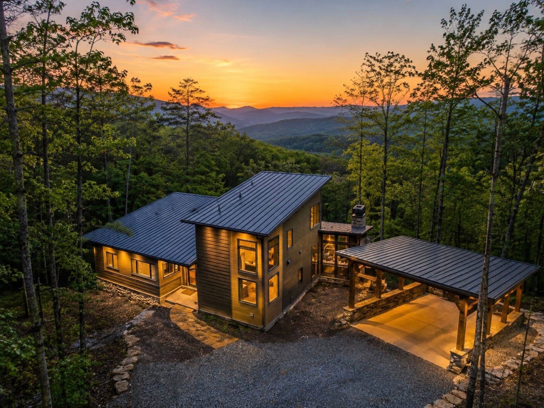 A modern cabin with a metal roof, surrounded by dense forest, and a view of the mountains in the background.