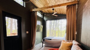 A modern interior with a wooden ceiling, a sofa, a small table, and large windows. - The Persimmon Tiny House at Cyprus Trail (Rockbridge)