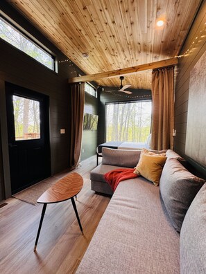Ein modernes Interieur mit Holzbalkendecke, einer Couch, einem kleinen Tisch und großen Fenstern.
