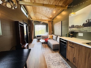 Een compact, modern interieur met een houten plafond, een bank, een eettafel en een keukenhoek.