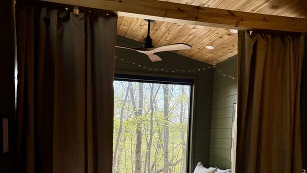 A bedroom with a large window, a bed, a sofa, and a ceiling fan. - The Persimmon Tiny House at Cyprus Trail (Rockbridge)