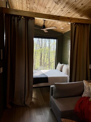 Een slaapkamer met een groot raam, een bed, een bank en een plafondventilator.