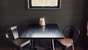 A table with two chairs, a pendant light, and a window with a view of trees. - The Persimmon Tiny House at Cyprus Trail (Rockbridge)