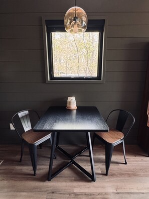 Ein Tisch mit zwei Stühlen, eine Pendelleuchte und ein Fenster mit Blick auf Bäume.