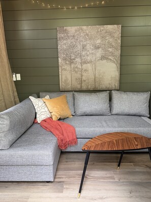 Een grijze hoekbank met gekleurde kussens, een rode plaid en een houten salontafel met zwarte poten.