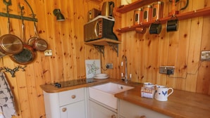 A wooden interior with a kitchen area including a sink, cabinets, and a microwave. - Bills Shepherds Hut (Brecon)