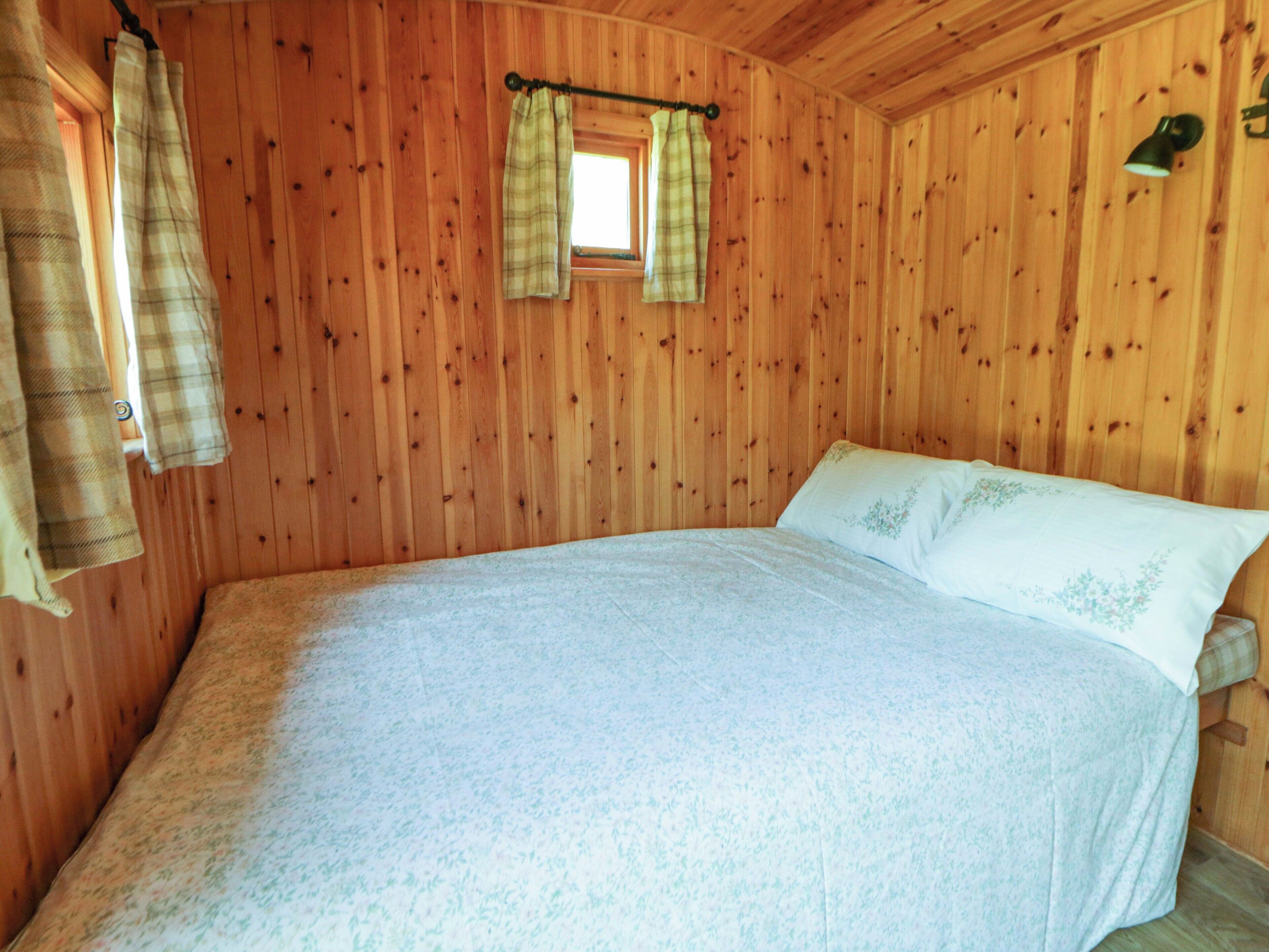 A wooden room with a bed, curtains, and a window.