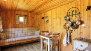 A wooden interior with a checkered sofa, dining table, chairs, and a kitchen area with hanging pots. - Bills Shepherds Hut (Brecon)
