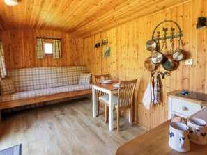 Puisesti sisustettu tila, jossa on ruutukuviollinen sohva, ruokapöytä, tuolit ja keittiöalue, jossa on katosta roikkuvia kattiloita.