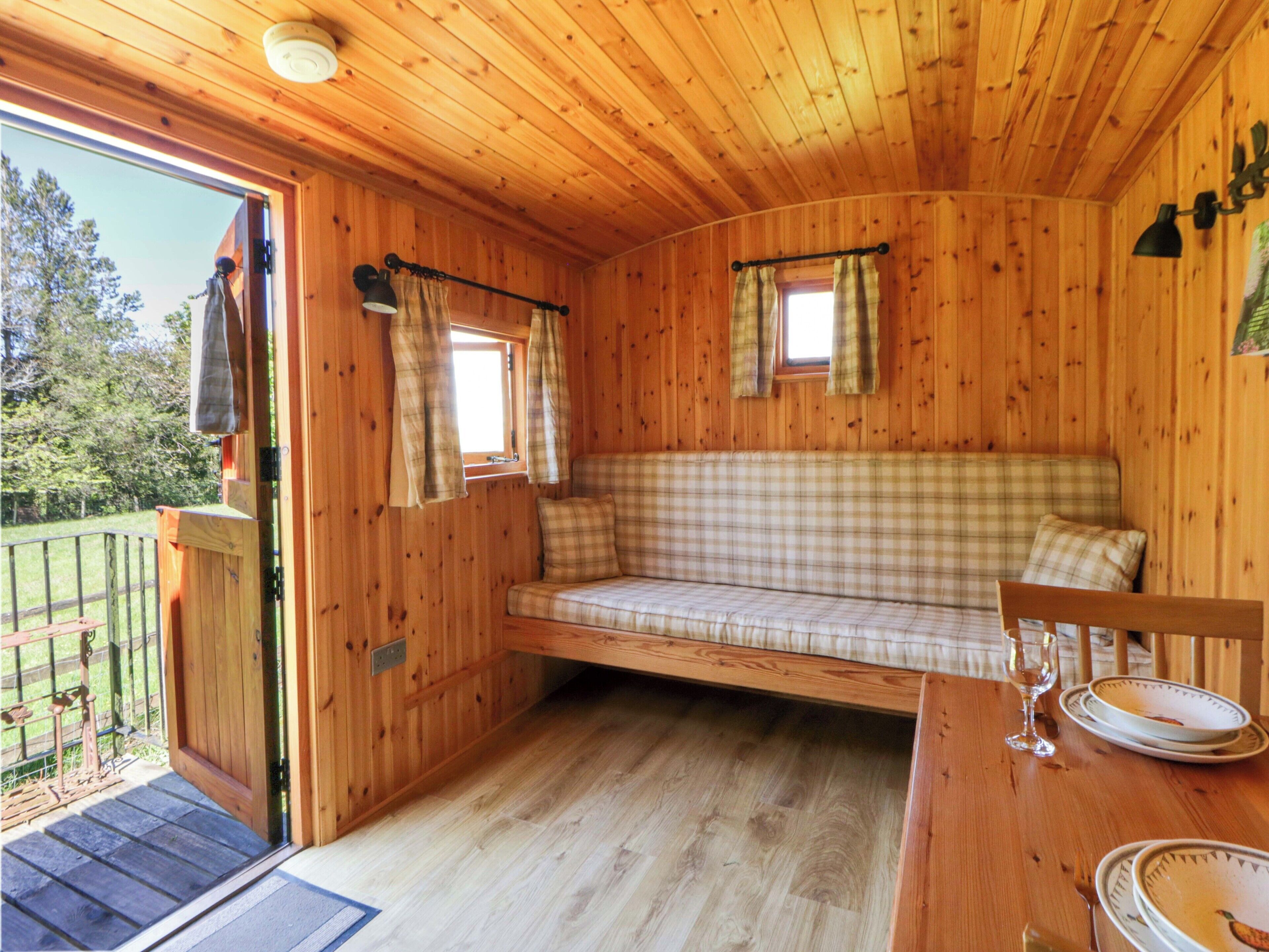 Ein Holzblockhaus-Innenraum mit einer Bank, einem Esstisch mit Tellern und einem Fenster mit Vorhängen.