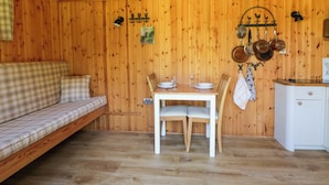 A wooden cabin interior with a sofa, dining table, chairs, and a kitchenette. - Bills Shepherds Hut (Brecon)