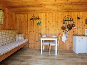 A wooden cabin interior with a sofa, dining table, chairs, and a kitchenette.