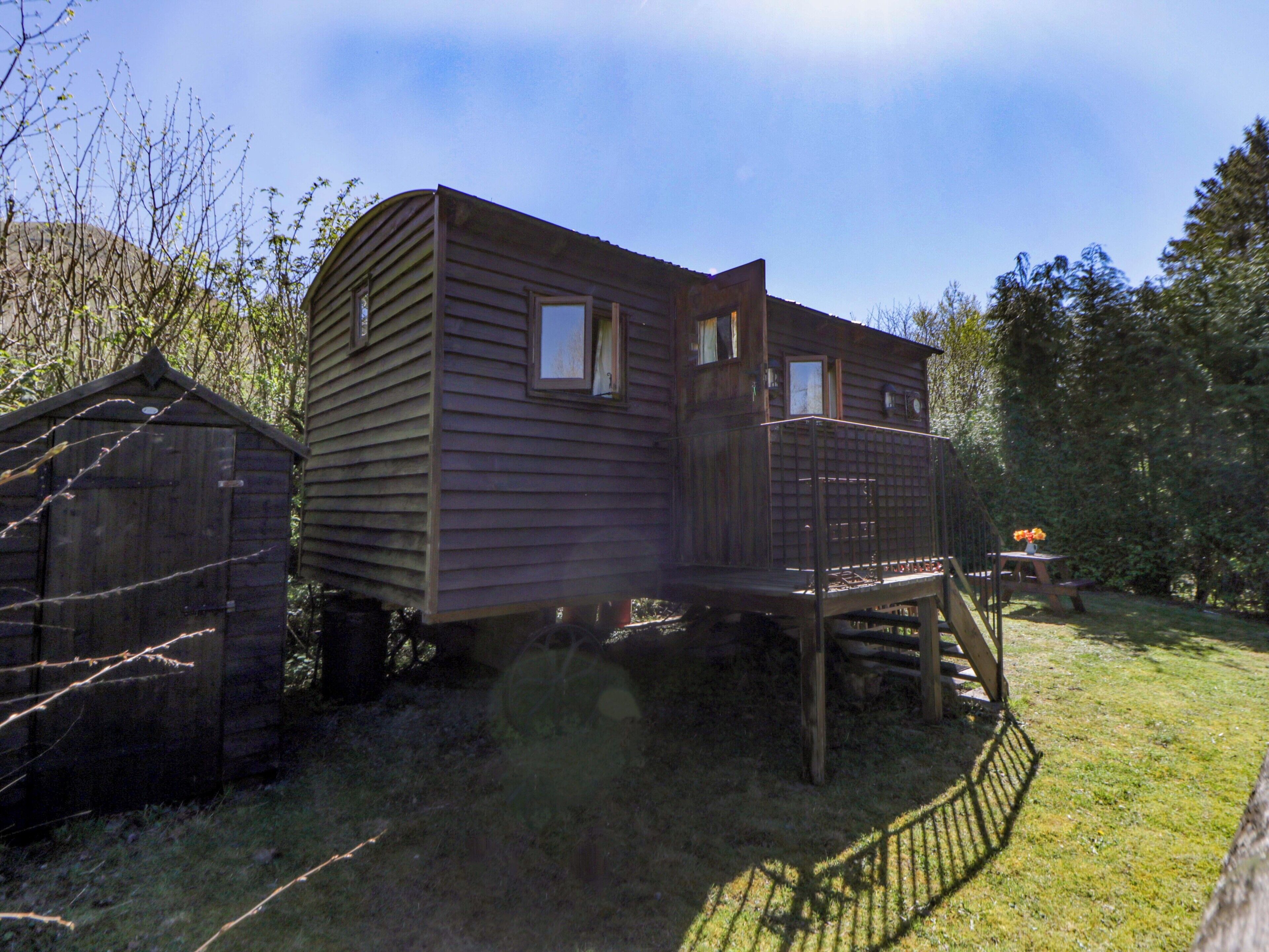 Une cabane en bois dotée d’une terrasse et d’un petit porche, entourée d’arbres.